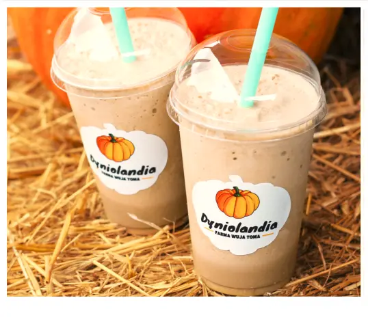 Pair of cold milkshakes with dome lids and straws, branded pumpkin logo visible, rustic setting.