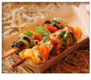 Three vibrant kebab skewers with peppers, zucchini and mushrooms served in a paper tray on straw